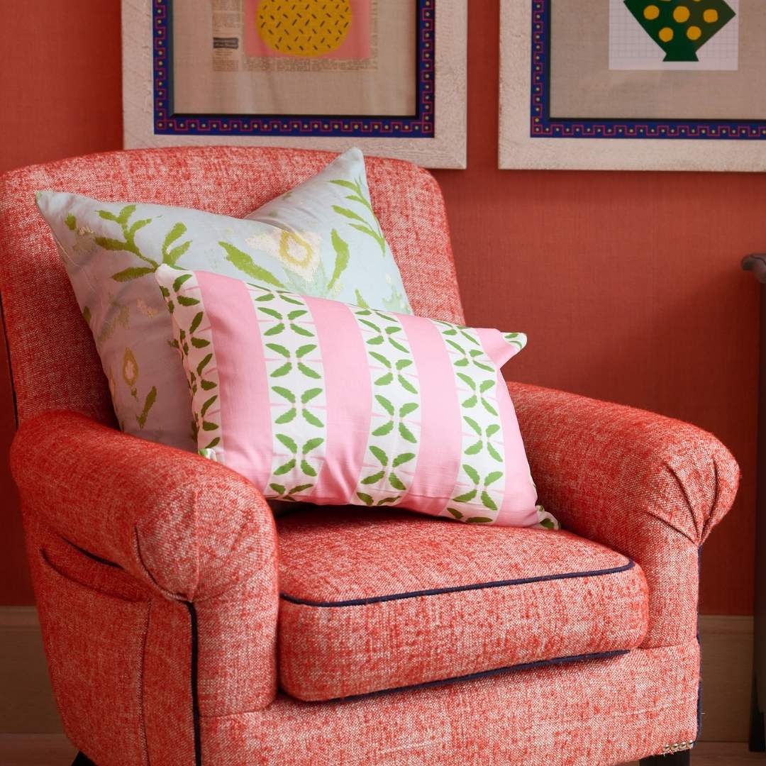 Laura Park Petal Stripe Pink decorative throw pillow with pink and white stripes and green leaf patterns styled with a petal garden aqua 22x22 throw pillow on a red accent armchair in a room with red walls with white frames containing abstract.