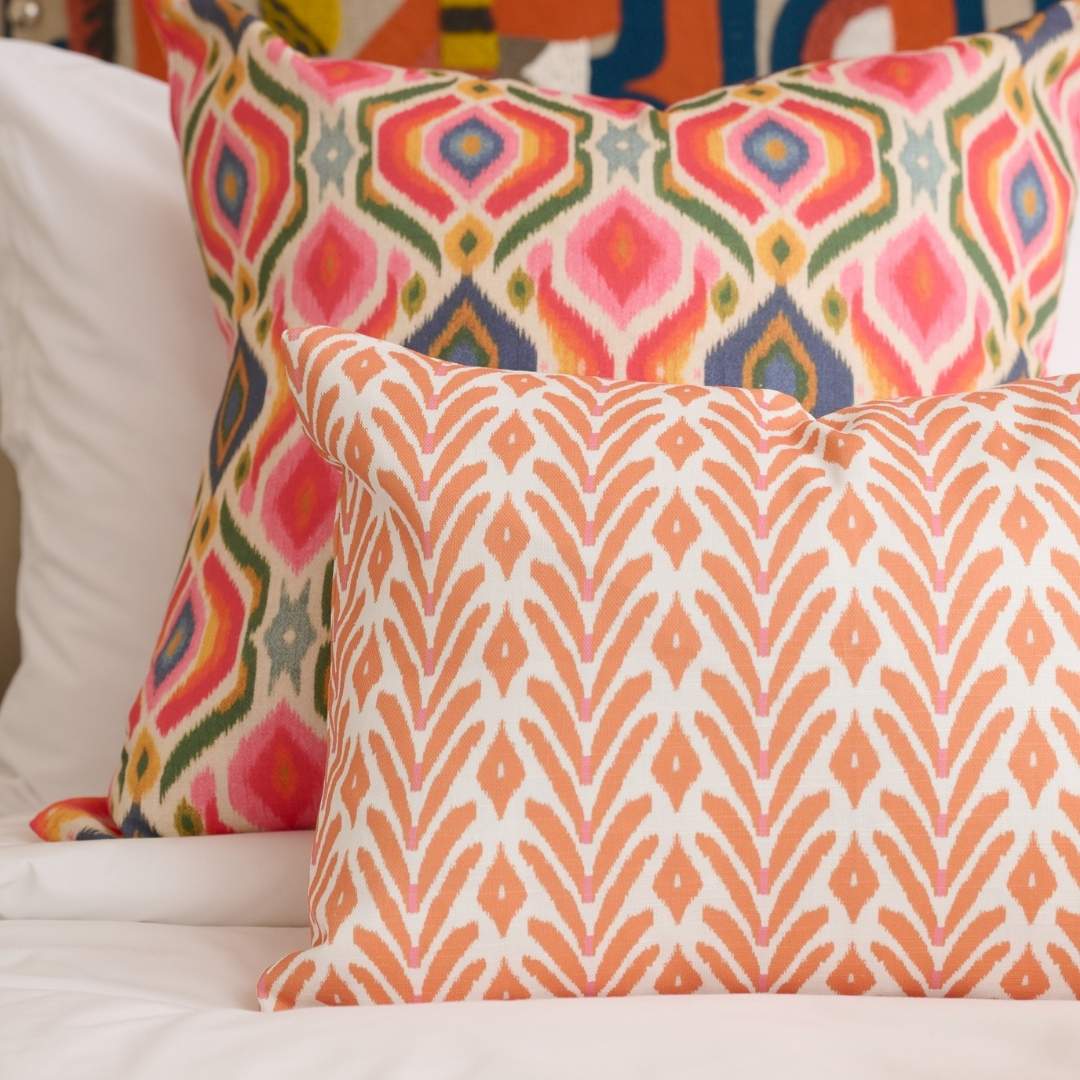 Decorative pillow with ikat inspired orange and white geometric painted pattern by Laura Park Designs styled on a bed with the Bloomsbury Ikat throw pillow. 