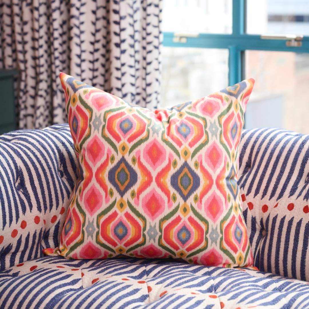 Bloomsbury Ikat decorative throw pillow by Laura Park featuring a colorful pink, blue, green, and yellow ikat print on a designer accent chair.