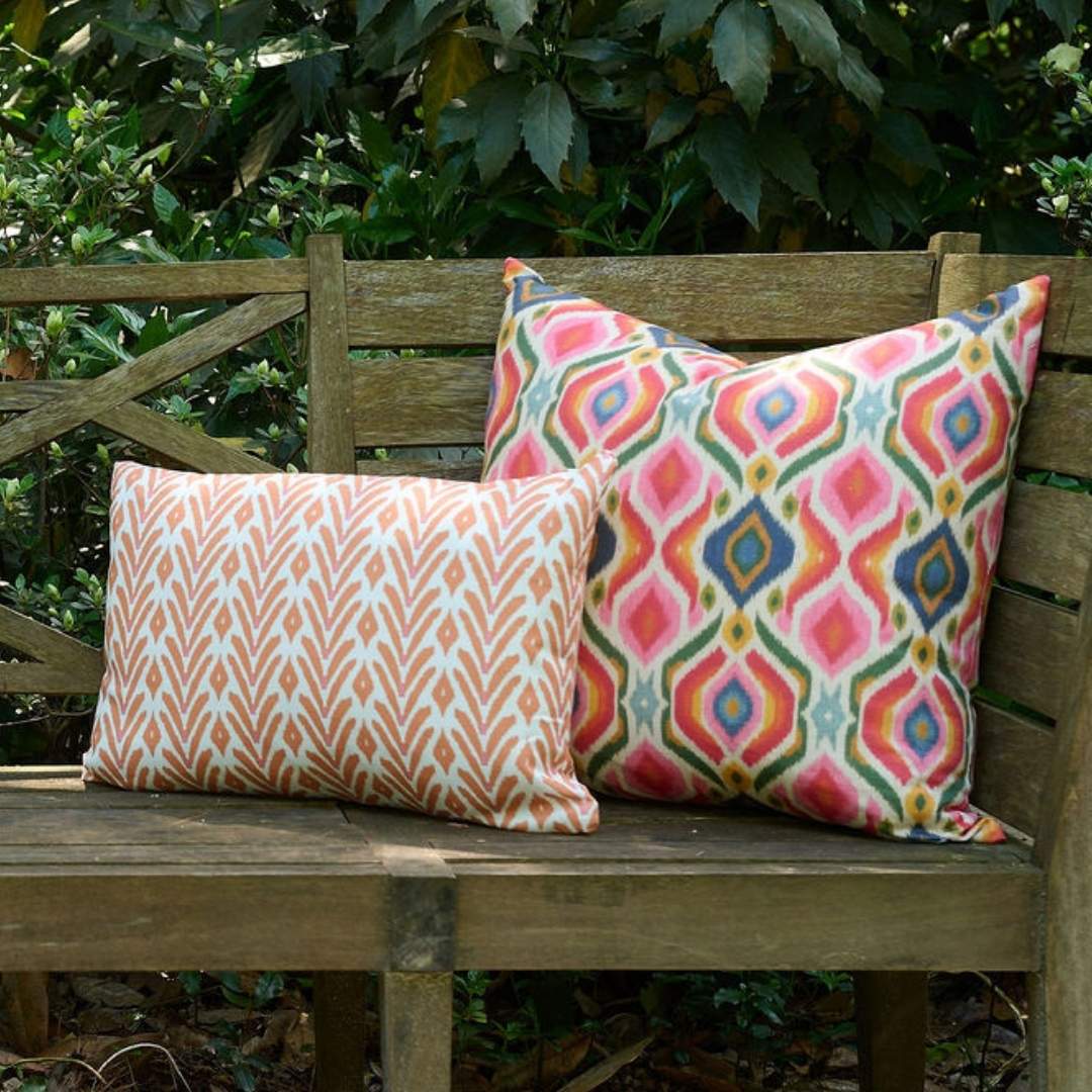 Bloomsbury Ikat outdoor decorative pillow by Laura Park with vibrant multicolor ikat pattern styled on a wooden patio bench for outdoor entertaining.