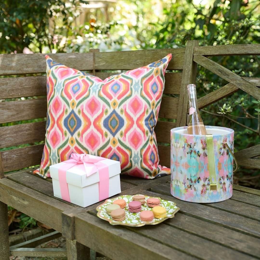 Bloomsbury Ikat outdoor decorative pillow by Laura Park with vibrant multicolor ikat pattern styled on a wooden patio bench for outdoor entertaining.