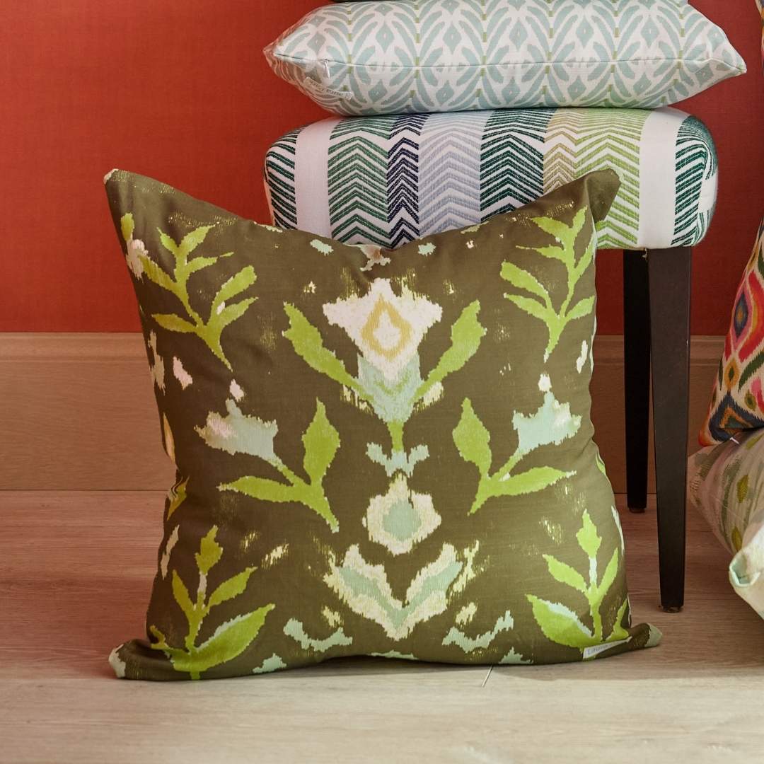 Petal Garden Olive decorative throw pillow by Laura Park Designs featuring hand-painted green and blue florals in light blue and green on a deep olive ground paired with Laura Park decorative pillows and an accent chair with a red painted wall.