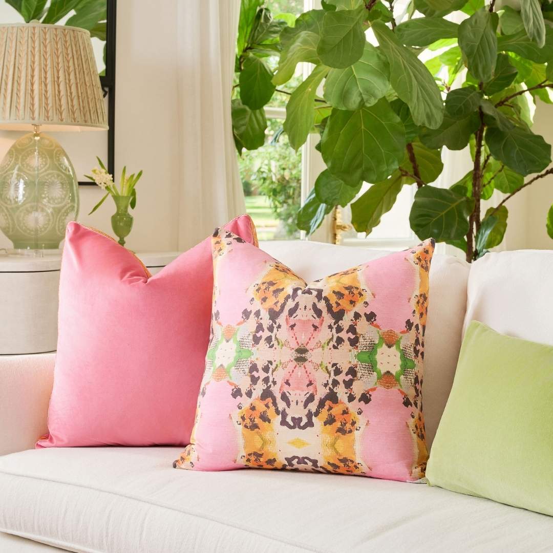 Laura Park's Tiger Lily Decorative throw pillow with bright pink orange and green with animal print accents styled on a light colored couch in a living room with a pink embroidered velvet pillow and green velvet lumbar pillow. 