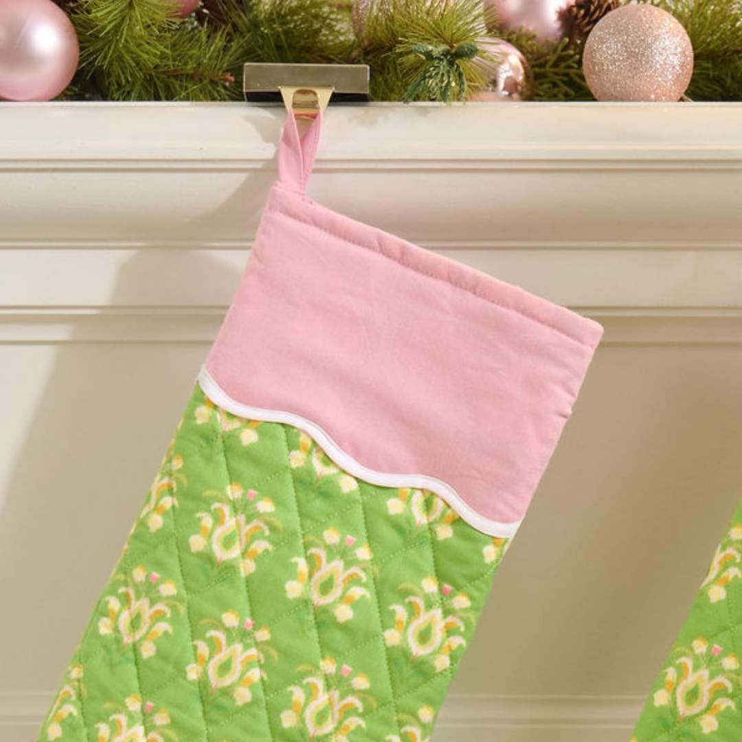 Green and pink quilted christmas stocking with a scalloped white detailing, the print is rosemary meadow, a green floral hand painted design by Laura Park, seen here on a mantle decorated with garland and pink ornaments. 