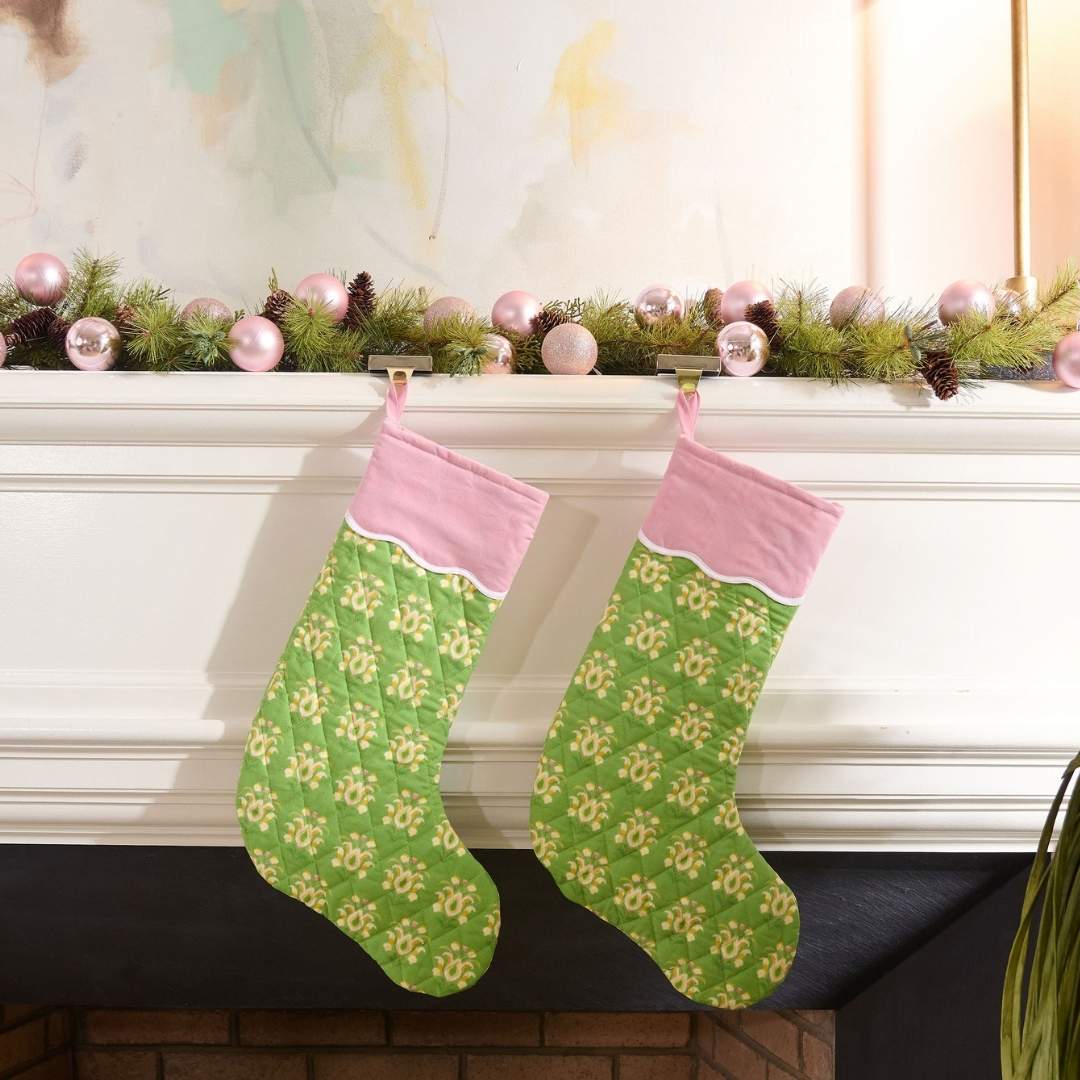 Green and pink quilted christmas stocking with a scalloped white detailing, the print is rosemary meadow, a green floral hand painted design by Laura Park hanging on a mantle with holiday garland and pink ornaments. 