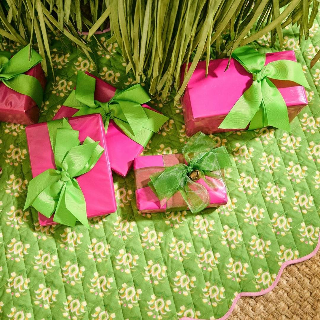 Pink wrapped christmas gifts under the tree with a laura park rosemary meadow green floral scalloped tree skirt with a pink scalloped lining. 
