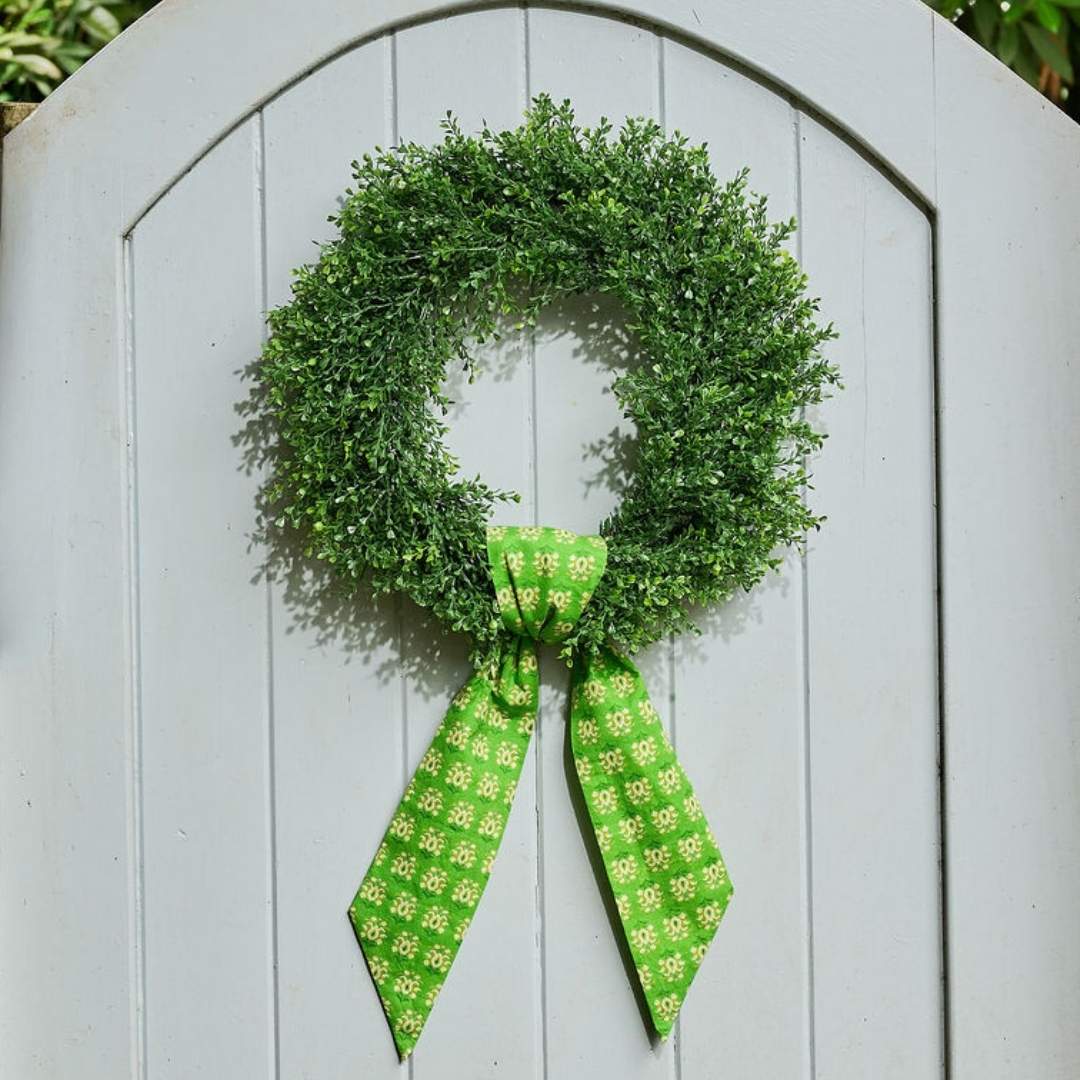 Green wreath with a matching green patterned wreath sash in Laura Park's signature rosemary meadow artful painted design on a grey fence door. 