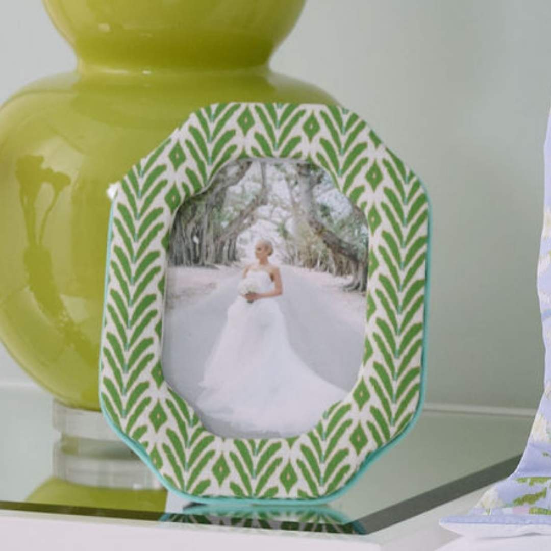 The Petite Frond Fabric Frame with ikat-inspired motif in bright green with subtle blue seen here with a bridal portrait inside the frame styled on a white bedside table next to a green contemporary lamp. 