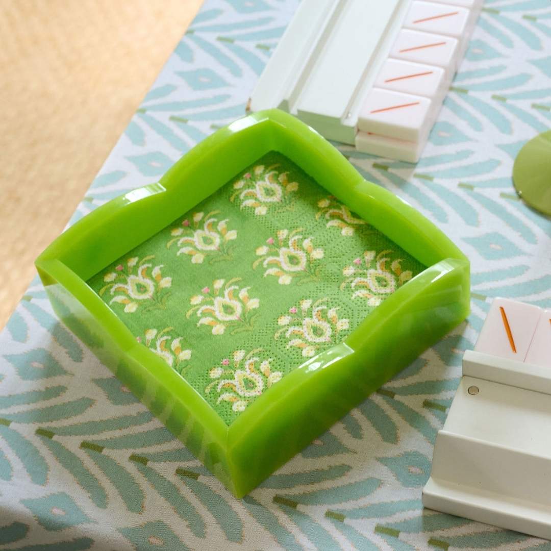 Laura Park paper cocktail napkins for entertaining and hosting in signature green painted floral pattern, rosemary meadow seen here on a mahjong table in a green acrylic scalloped cocktail napkin holder. 