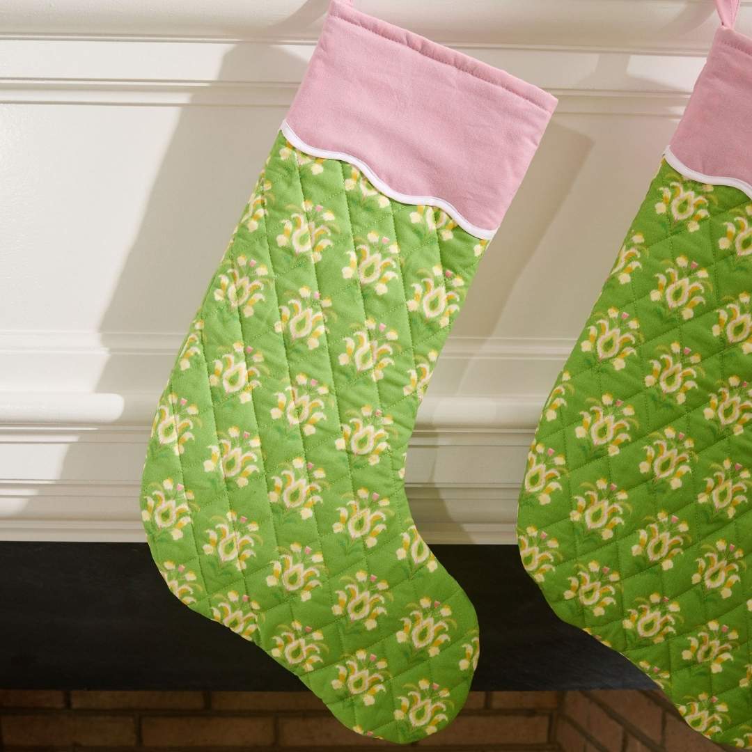 Green and pink quilted christmas stocking with a scalloped white detailing, the print is rosemary meadow, a green floral hand painted design by Laura Park hung on a fireplace mantle ready for holiday celebration.