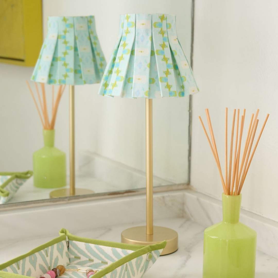 Chloe Blue box pleat lamp shade cover by Laura Park with a hand-painted floral pattern in shades of blue, cream, and olive on a bathroom counter paired with a snap tray. 
