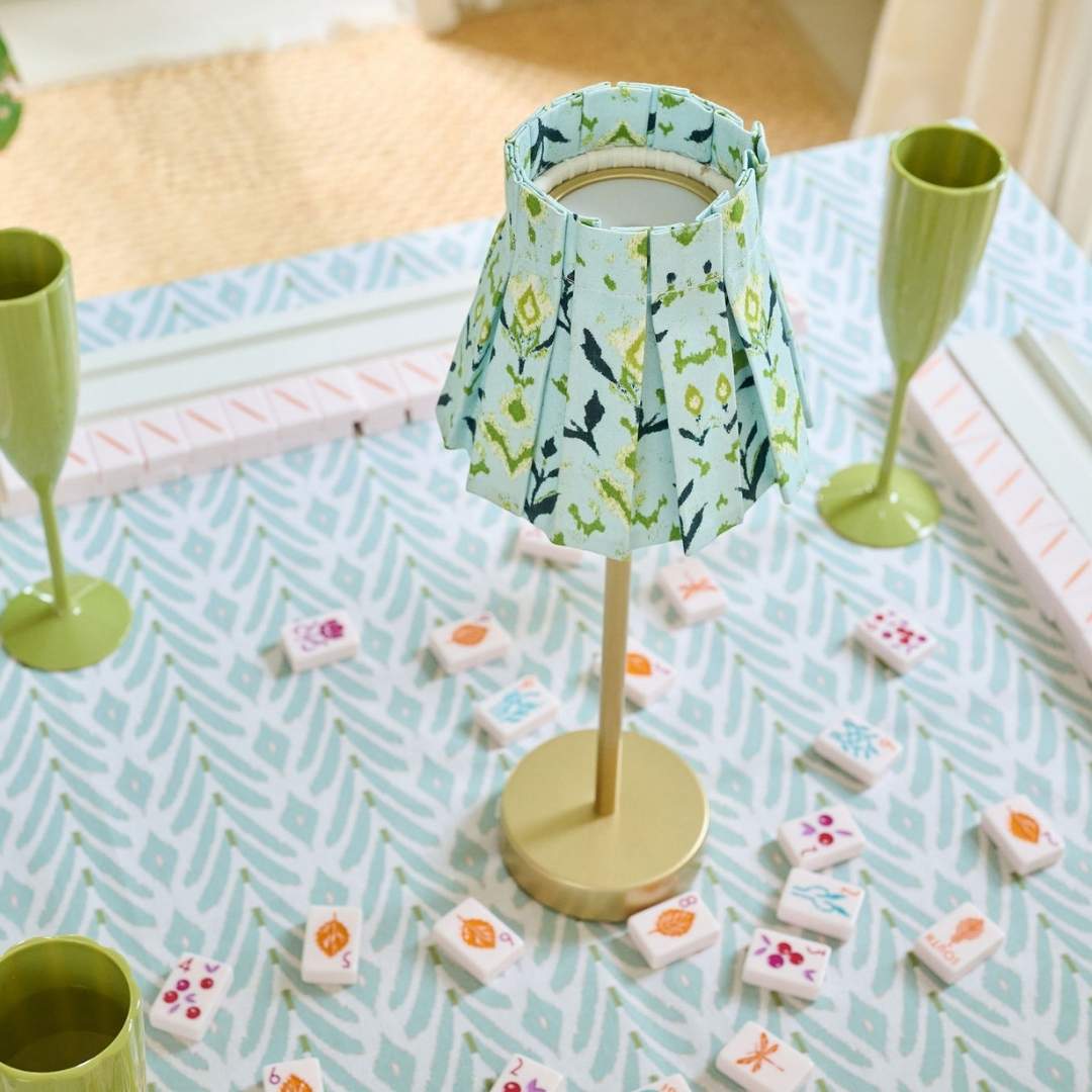 Laura Park's pleated and hand painted green, navy, and light blue lampshade slipcover in petal garden navy by laura park, styled on a mahjong table with green acrylic champagne flutes.