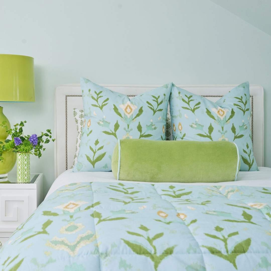 blue, green, and white hand painted floral and leaf patterned bedding set designed by Laura Park pillows, lamp, and vase in the background, styled for a guest room, bedroom, or dorm room. 
