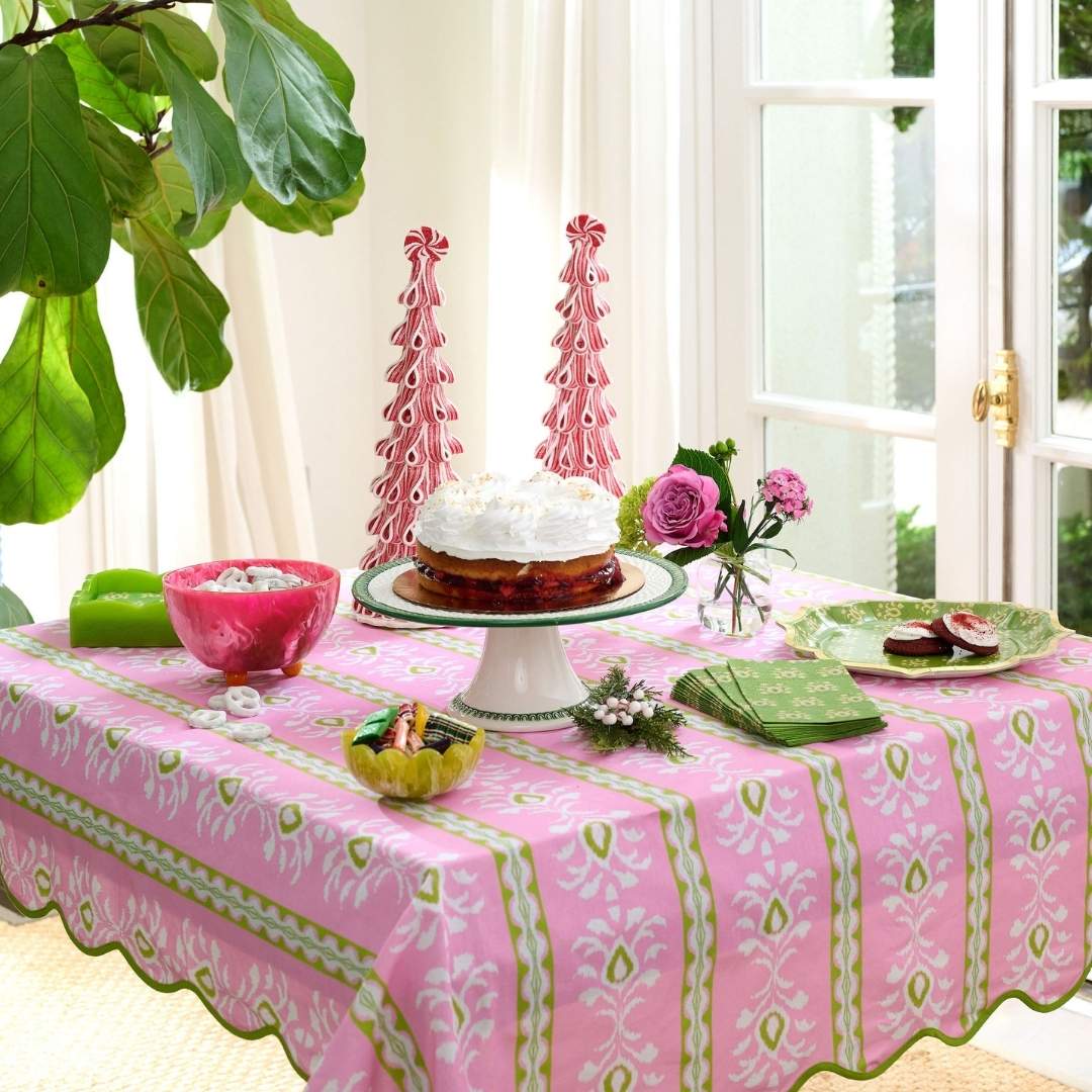 Laura Park Rosemary Stripe Pink tablecloth with green and white floral pattern and a green scalloped edge on a table set with pe3ppermint christmas trees, rosemary meadow scalloped dinner plates and guest towels, and green, pink, and yellow.