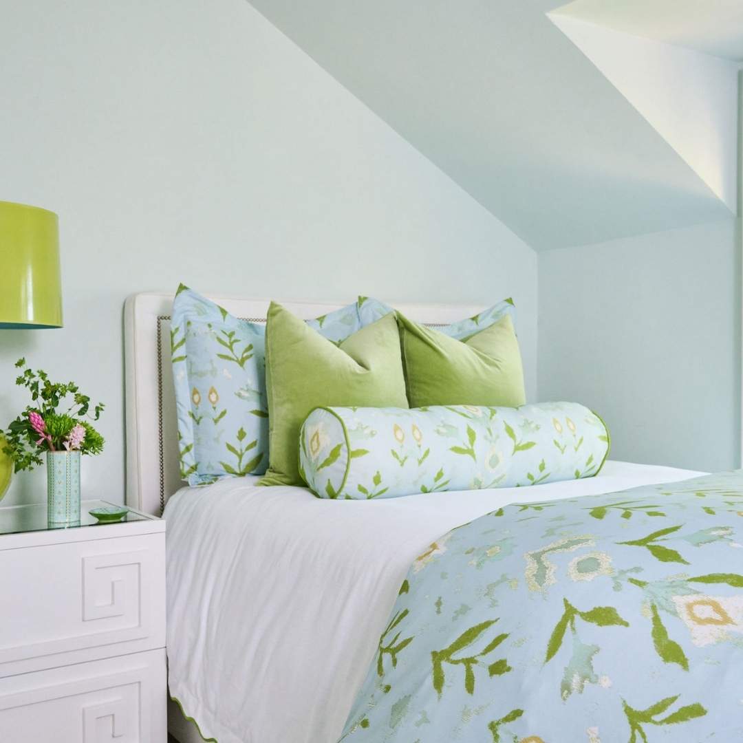 Petal Garden Aqua pillow shams by Laura Park Designs with green hand painted leaf pattern on a light blue background styled on a white bed with green velvet pillows and a petal garden bolster pillow. 
