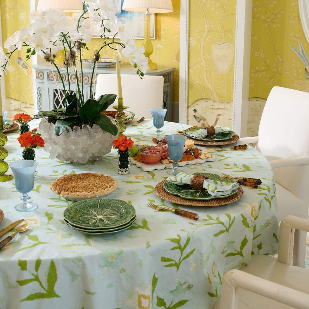 Round tablecloth with Laura Park's signature Petal Garden Aqua floral pattern on a white background, perfect for dining rooms or entertaining. Seen here with a table set for guests with coordinating plates, cups, utensils, and napkins. 
