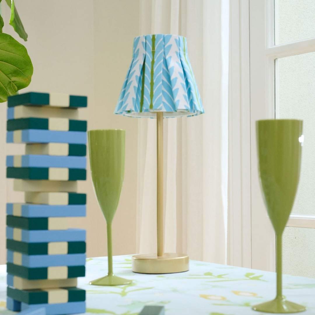 Garden Party scalloped acrylic champagne flutes in green by SumnerEdit and Laura Park Designs styled with a decorative lamp with a blue and green patterned shade.
