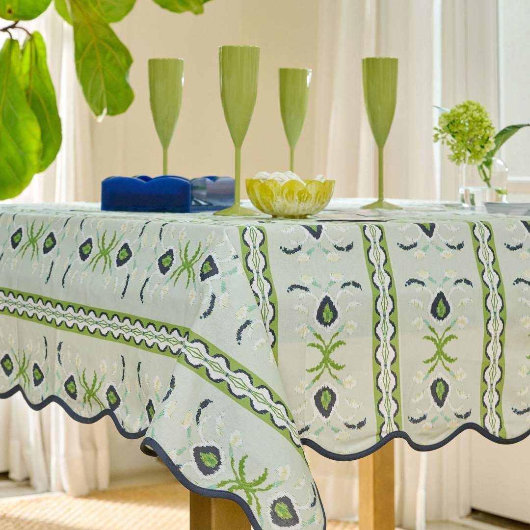 table set with the laura park rosemary stripe lagoon scalloped game table cloth for a square table with light blue, navy, and green floral accents and a navy scalloped edge. on the table are the acrylic napkin holder, four green champagne.