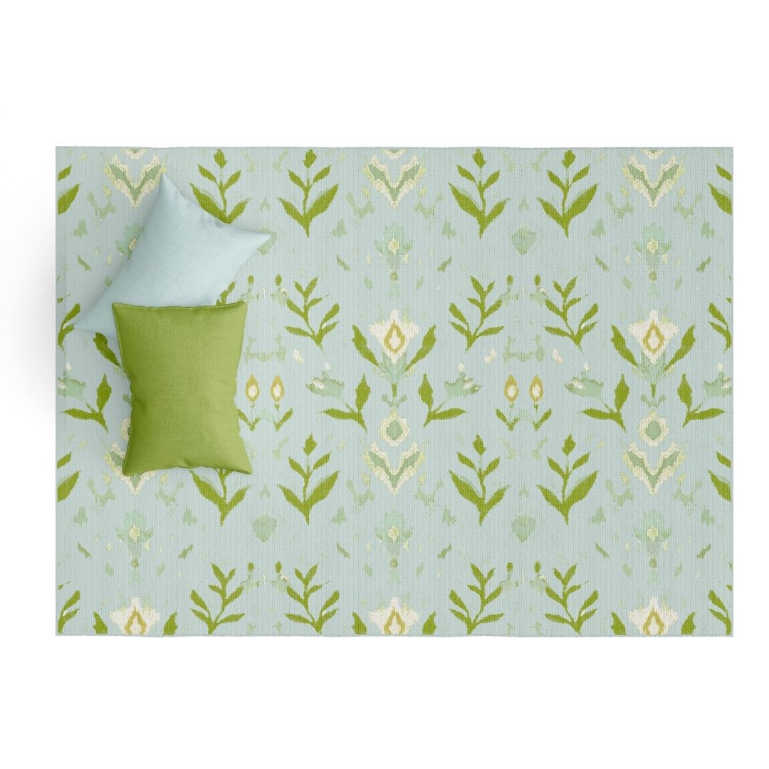 Laura Park's Signature painted pattern, petal garden aqua on a floor mat rug for indoor use in kitchen, bathroom, entry room, mud room, bedroom. Styled with a blue and green pillow. 