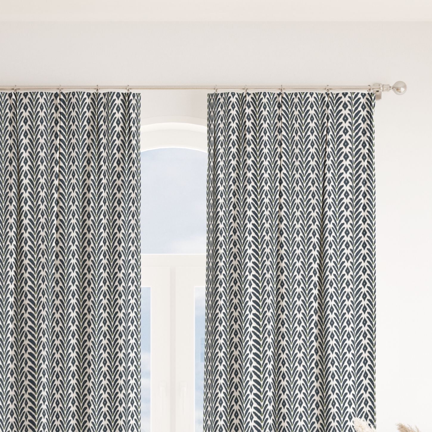 Pair of ikat inspired laura park petite frond navy pinch pleat curtains on a silver curtain rod over a large arched window. 
