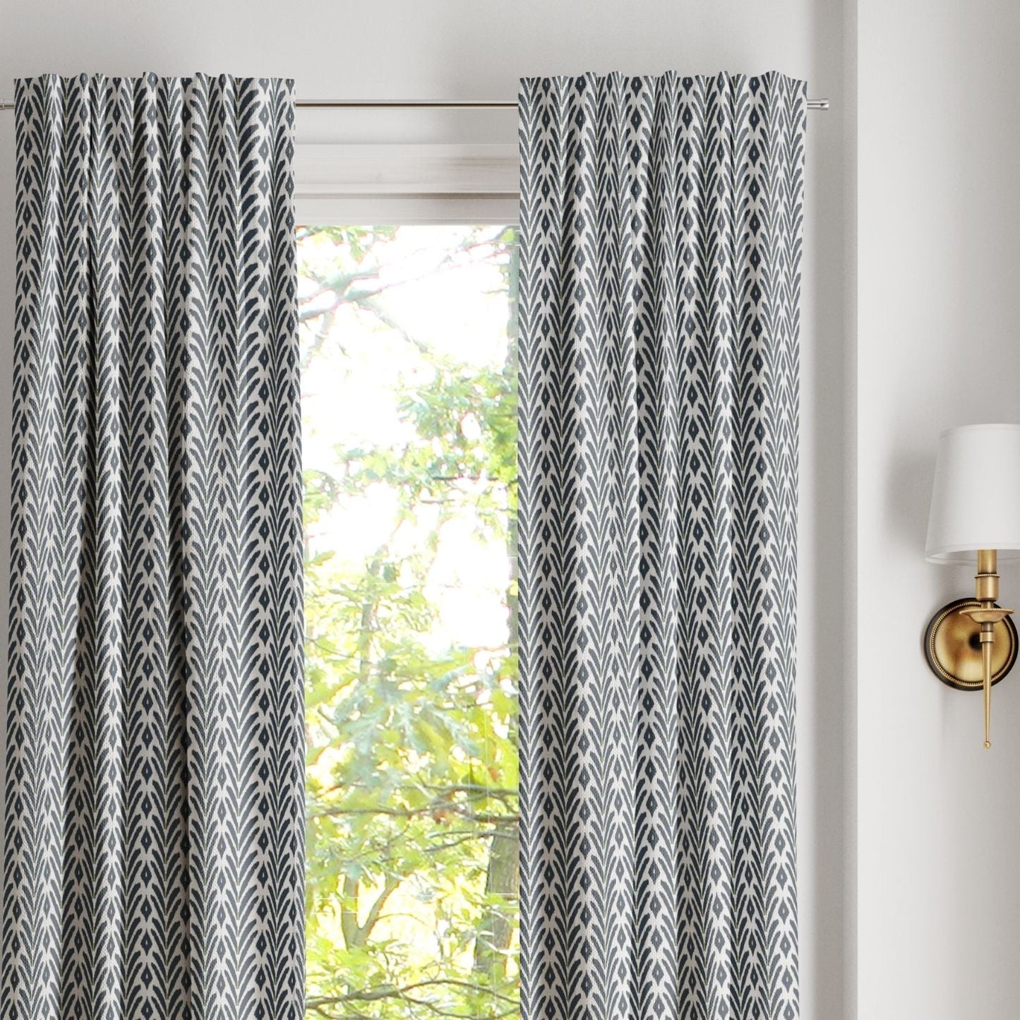 Pair of ikat inspired laura park petite frond navy rod loop curtains on a silver curtain rod over a large arched window. 