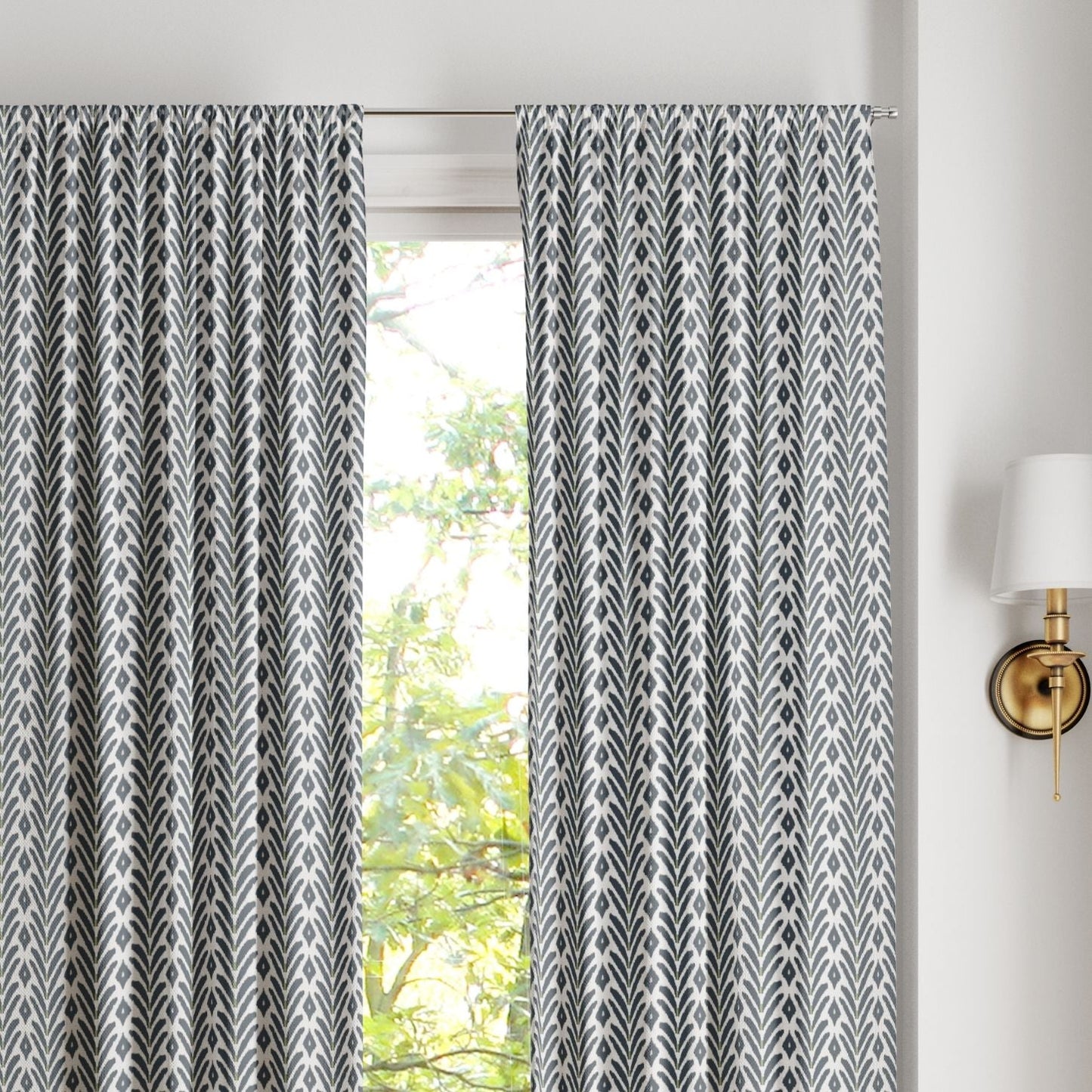 Pair of ikat inspired laura park petite frond navy rod pocket curtains on a silver curtain rod over a large arched window. 
